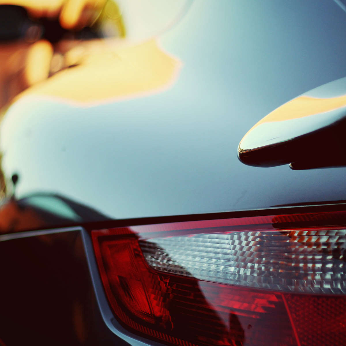 Close-up of a car's rear light with sleek, glossy bodywork reflecting sunlight.