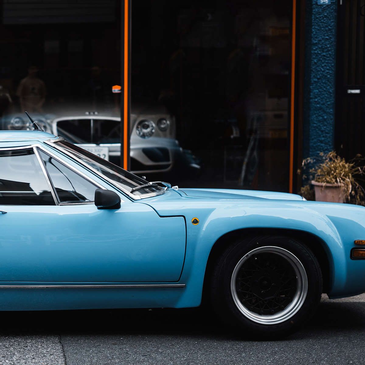 Classic blue sports car parked near a café window.