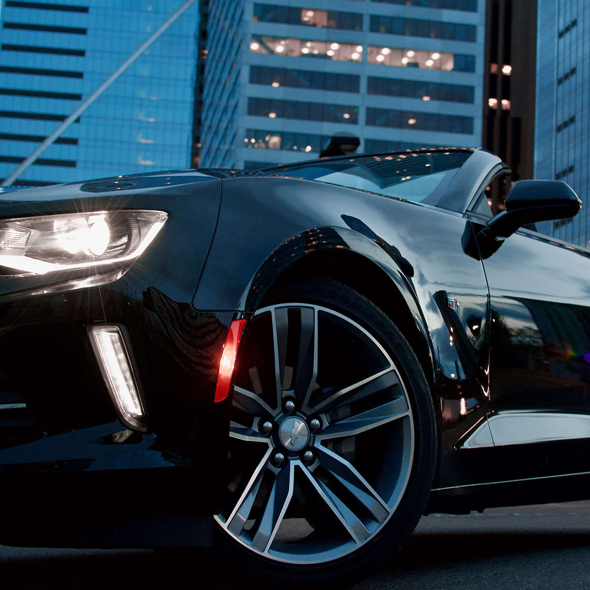Close-up of a sleek black sports car wheel and headlight at dusk.