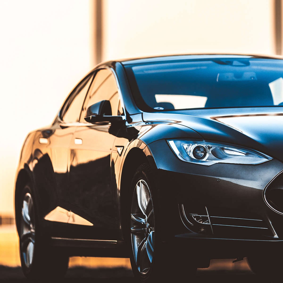 Sleek black luxury car parked indoors with sunlight reflections.