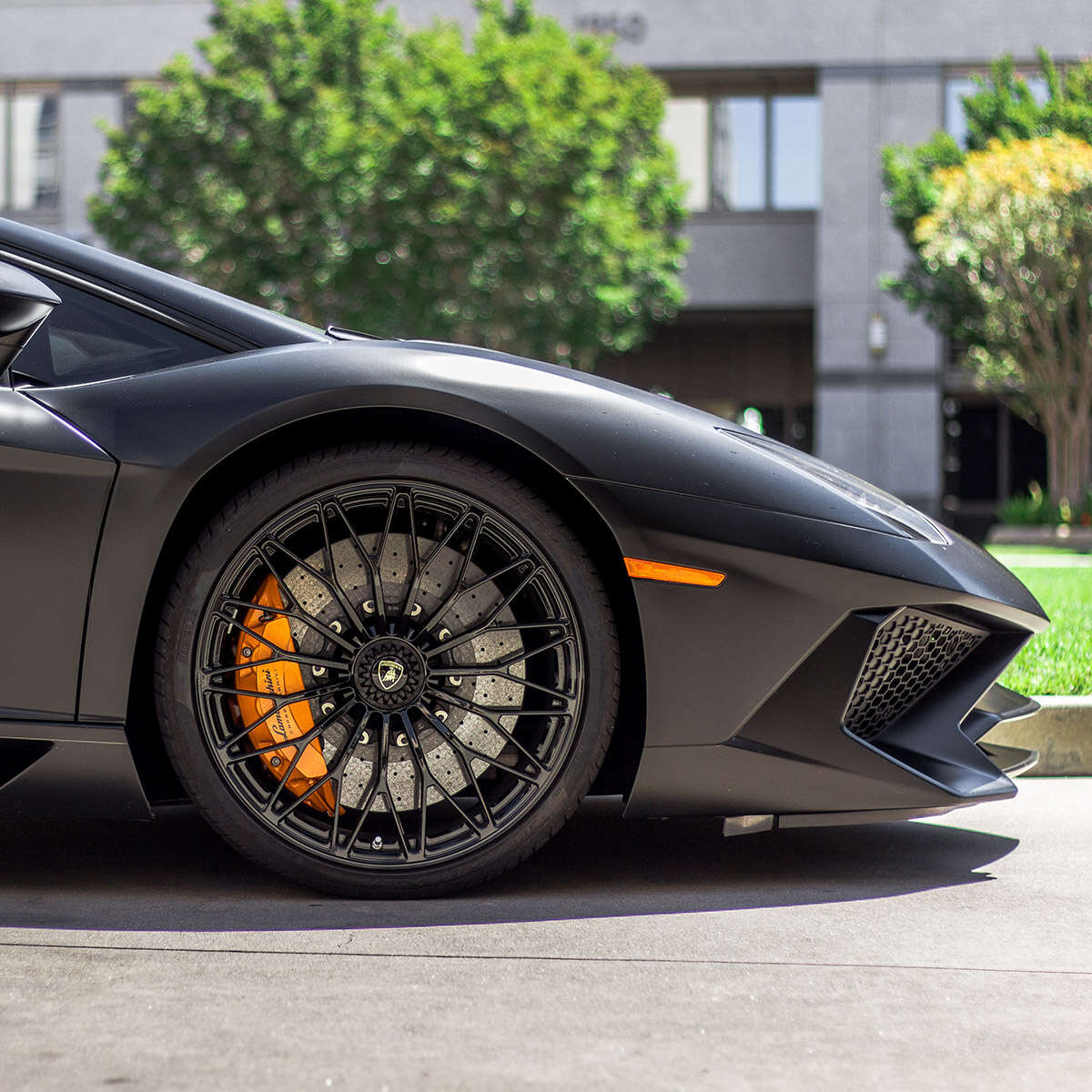 Close-up of a sleek black sports car front wheel with orange brake calipers.